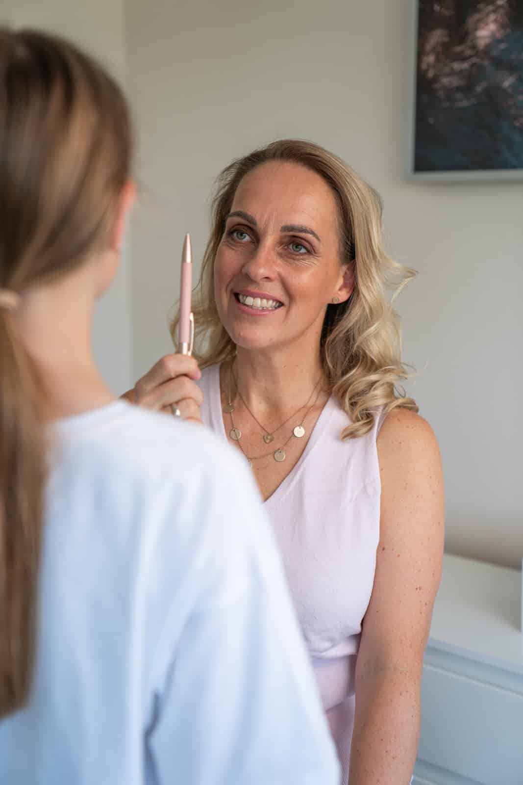 Juliane Danziger hält einen rosa Stift hoch und lächelt eine junge Patientin an, die mit dem Rücken zur Kamera vor ihr steht.